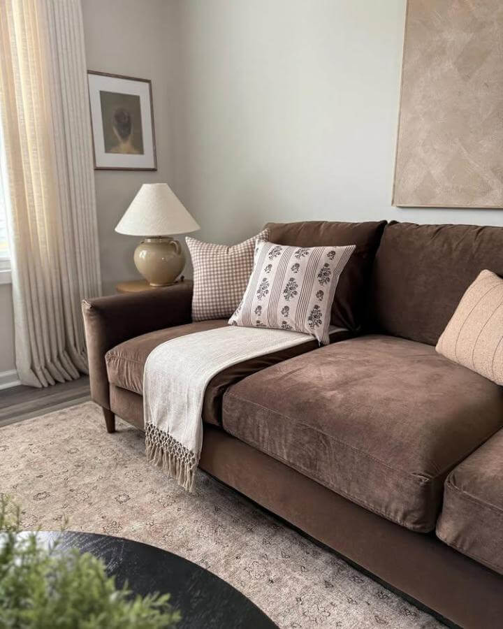 Dark brown velvet couch with neutral beige pillows and throw styled in cozy living room by @kaylascurated.