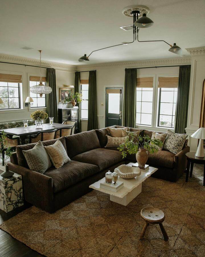 Dark brown velvet couch with layered cushions and jute rug in a warm, inviting living room by @arceriinteriors.