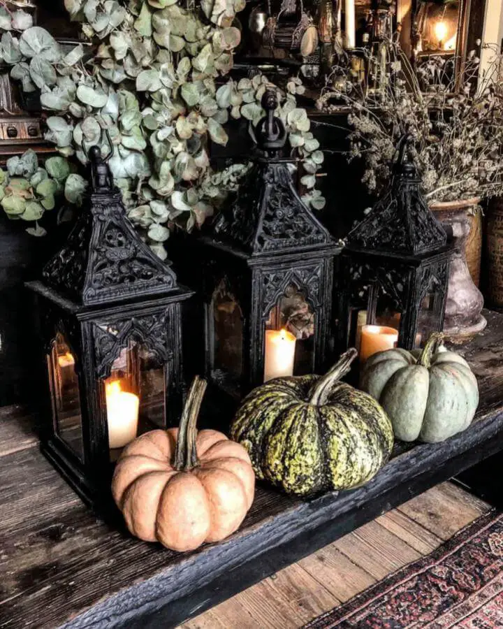 Gothic black lanterns with candles and muted pumpkins showcasing dark fall decor ideas on rustic wooden mantel.