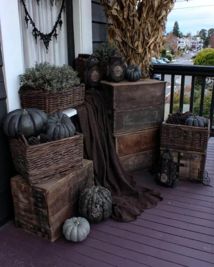 Rustic wooden crates and wicker baskets arranged on porch with gray pumpkins and corn stalks.