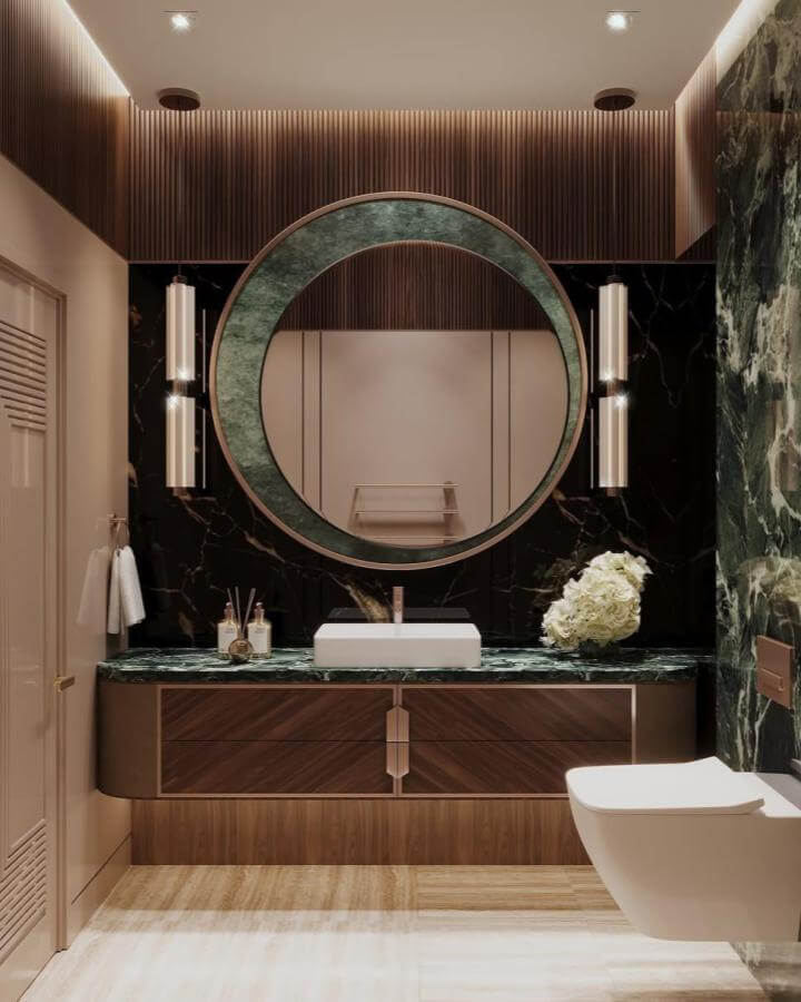 Dark green powder room with round marble mirror, wooden vanity, and ambient lighting by @thehauteinteriors showcasing rich textures.