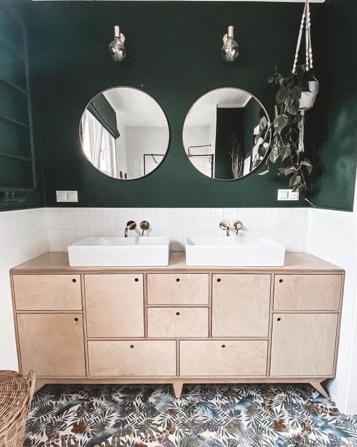 Dark green powder room with natural wood vanity, round mirrors, matte gold fixtures, and botanical floor from @fortheloveofply. Balanced and stylish.