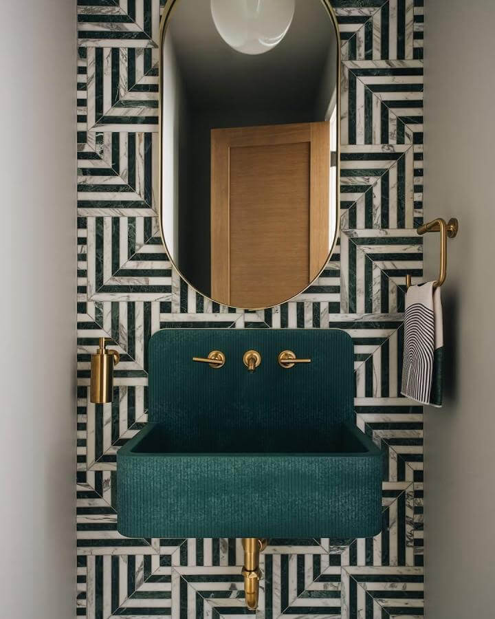 Dark green powder room with geometric marble tiles, ribbed sink, and brass fixtures from @amystormandco enhancing texture and contrast