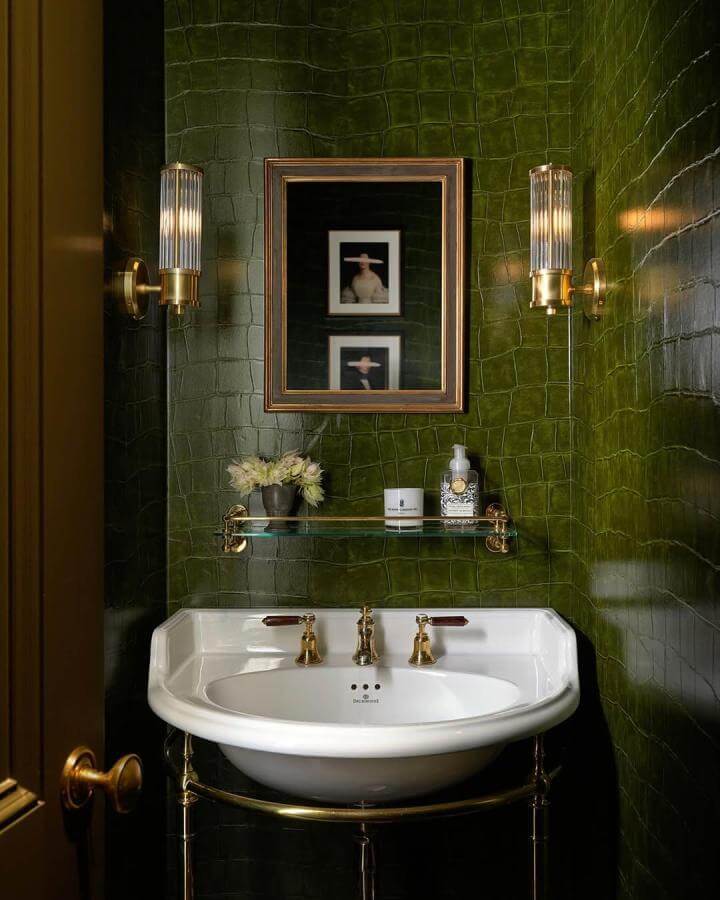 Glossy dark green crocodile-textured walls with gold accents in a powder room from @seanlitchfield. Classic white basin and elegant lighting.