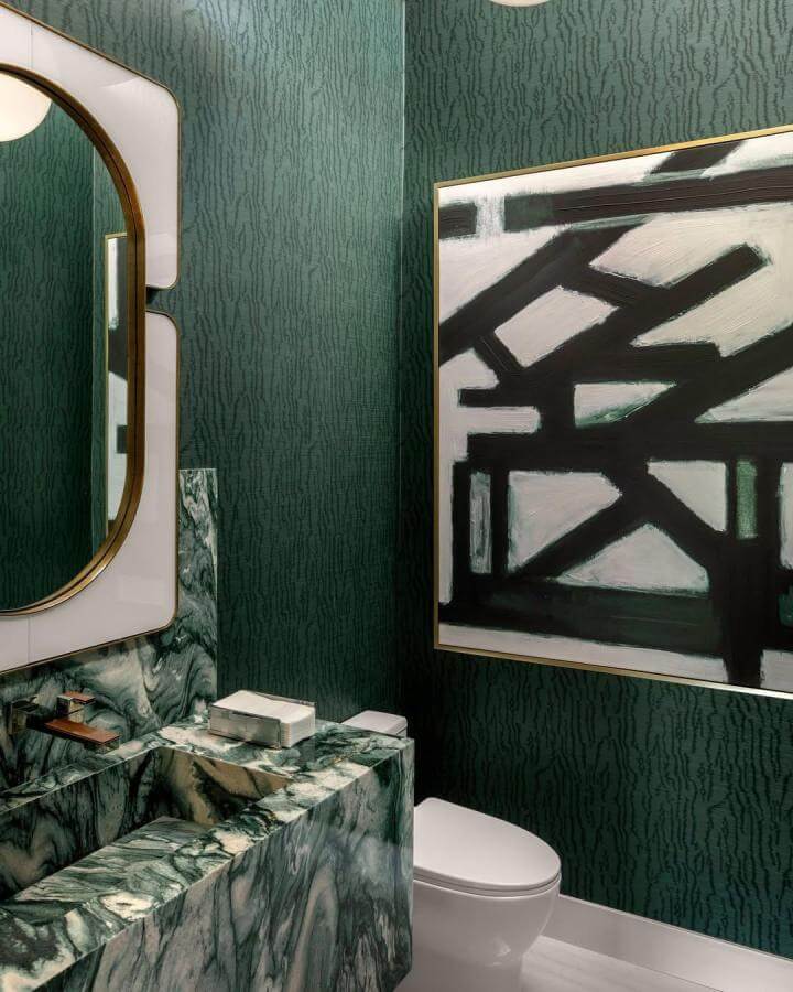 Dark green powder room with marble sink, textured wallpaper, gold framed mirror, and abstract black and white art.