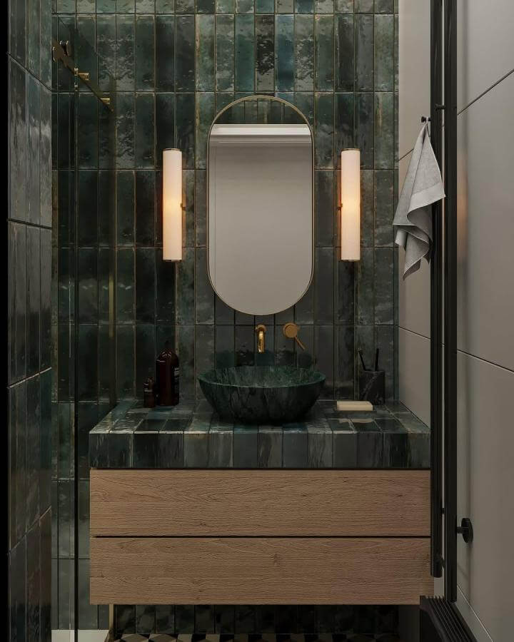 Dark green glossy textured tile powder room with brass accents and wooden vanity from @designminimal.nl showcasing rich material contrast.
