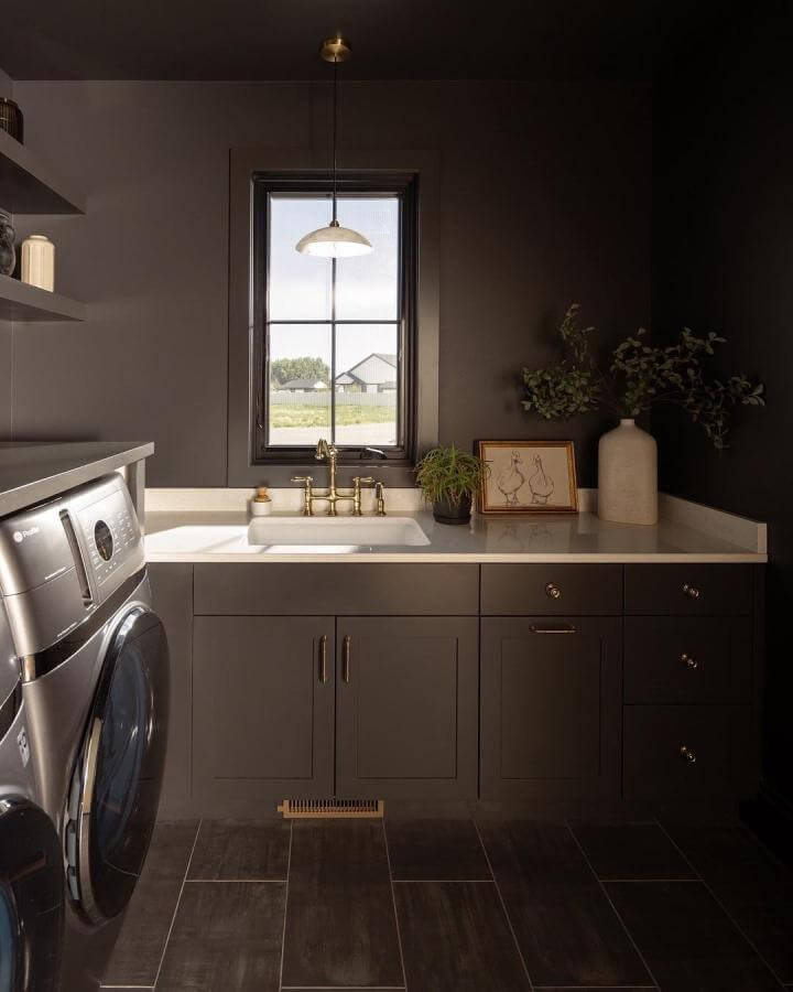 Matte charcoal cabinetry laundry room with white quartz counters and brass hardware by @hannessonhome creating a cozy, stylish space.