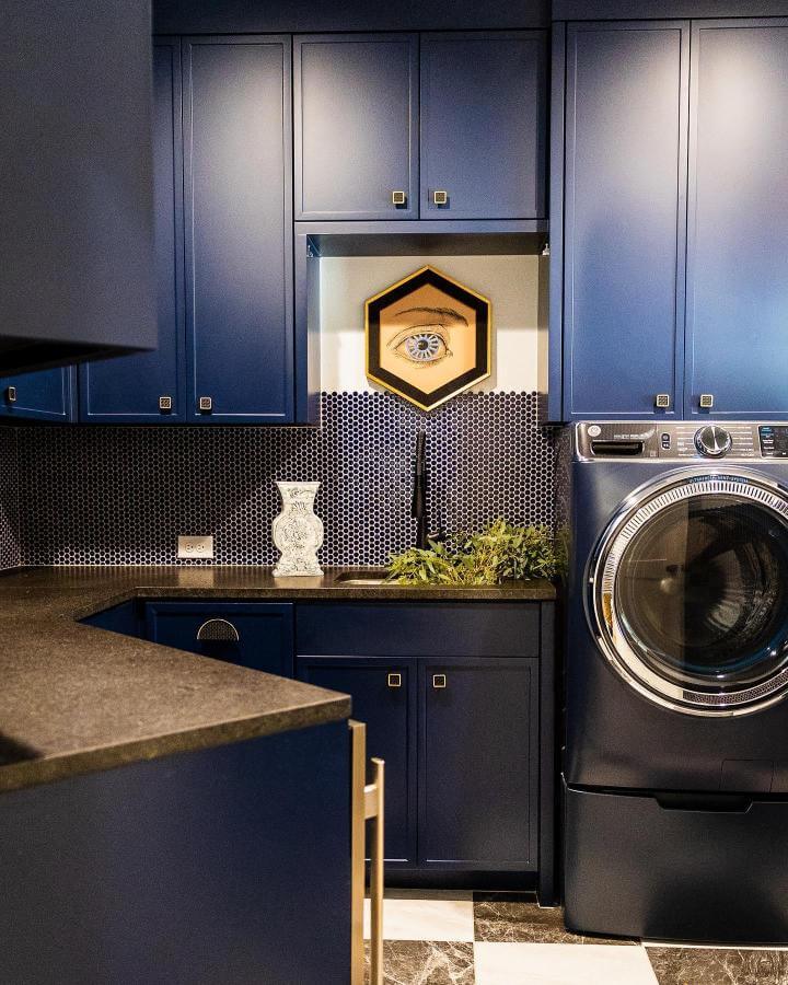 Navy cabinetry with hexagonal tile backsplash in a modern laundry room by @janaschleifinteriors. Stylish and cozy dark design.