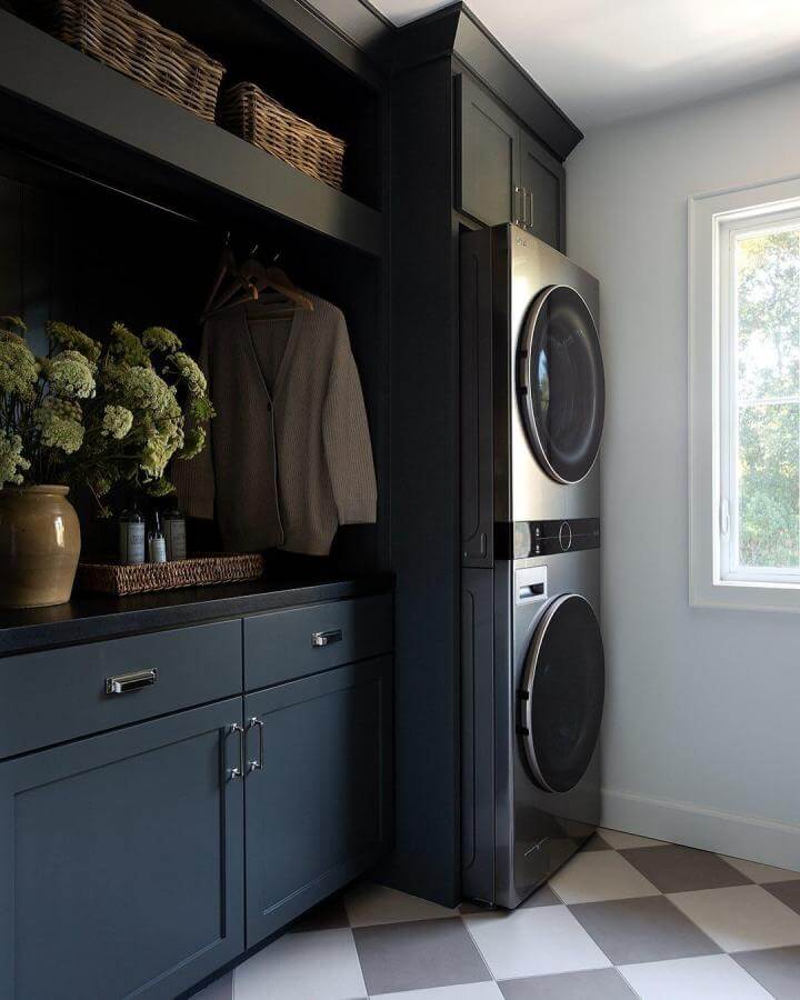 Dark black cabinetry laundry space with stacked silver washer dryer and natural light by @twigandoakdesign showing chic organization and contrast.