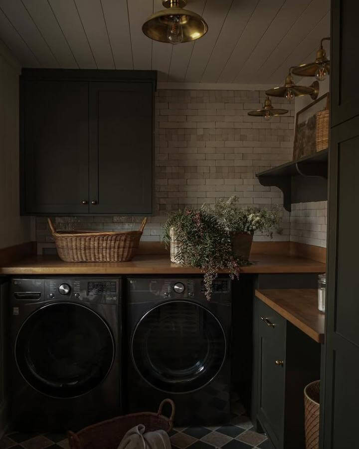 Matte black washer and dryer set with charcoal cabinets and wooden accents in a warmly lit laundry room by @maggievollrath.