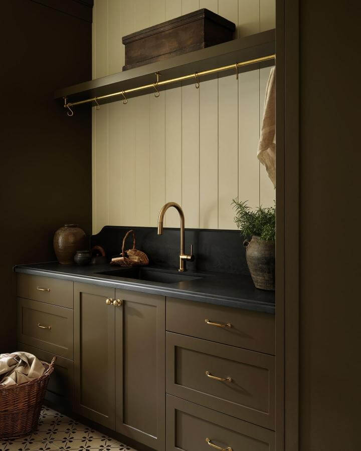 Olive cabinetry laundry nook with brass hardware and faucet by @tiffanyleighdesign showing cozy dark decor and natural accents
