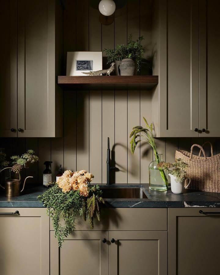 Olive green cabinetry laundry room with dark stone countertop and black faucet by @bluelinecustombuilders featuring natural decor accents.