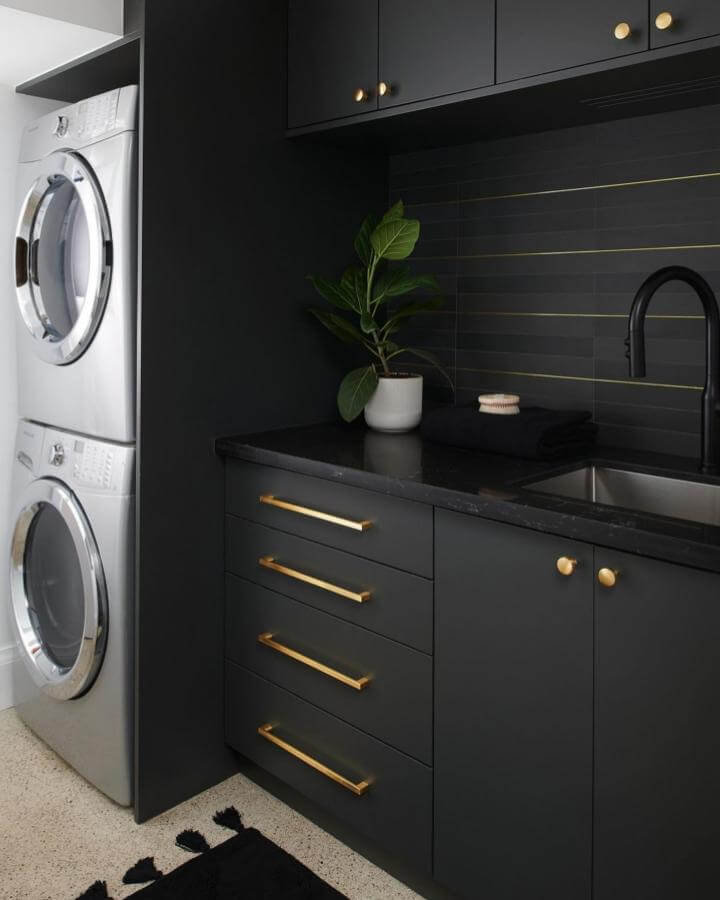 Dark matte cabinetry laundry space with gold hardware and black tiles from @thehouseoftori. Modern, cozy contrast and clean lines.