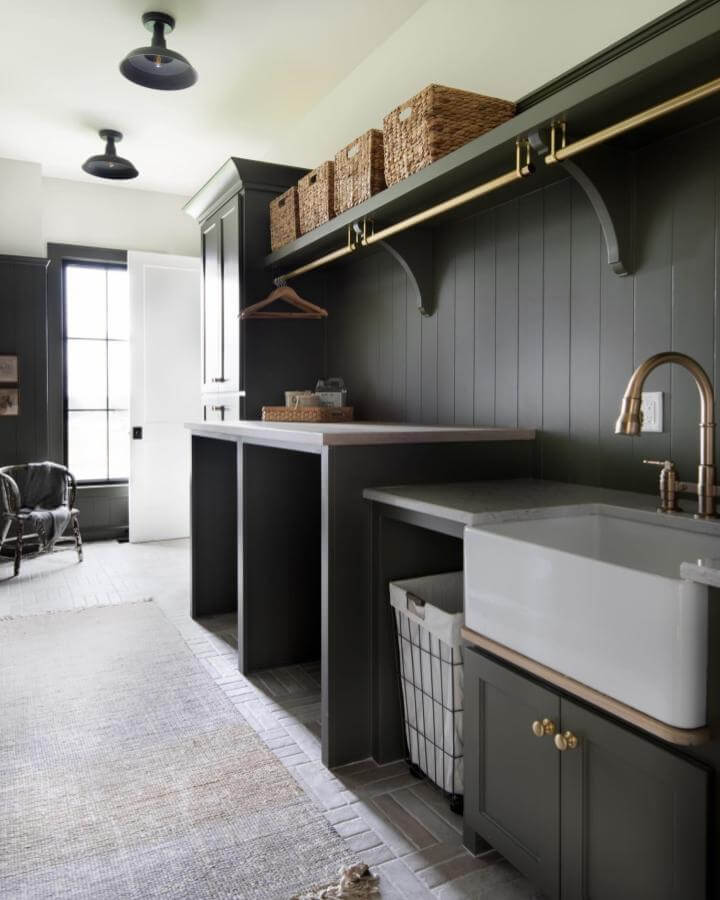 Dark olive cabinetry laundry room with brass accents and natural woven baskets from @cardinalcrestkc showcasing dark laundry room ideas with farmhouse sink and organized storage.