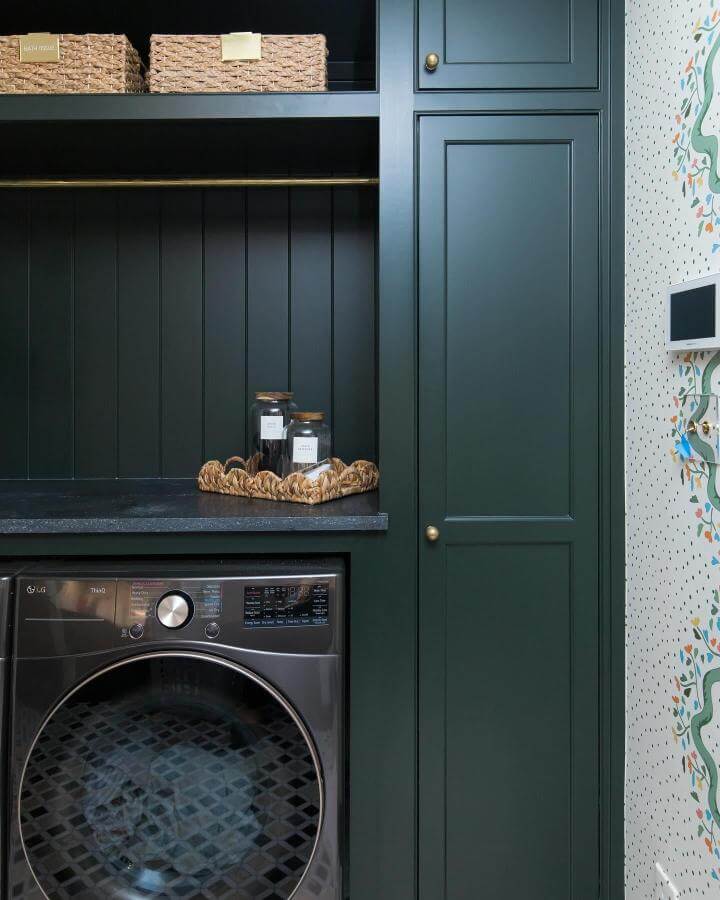 Dark forest green cabinetry laundry room with brass accents and natural woven baskets by @soshomeorganization, cozy and stylish utility space.