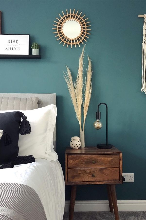 A minimalist room with teal walls and boho-style decor accents.