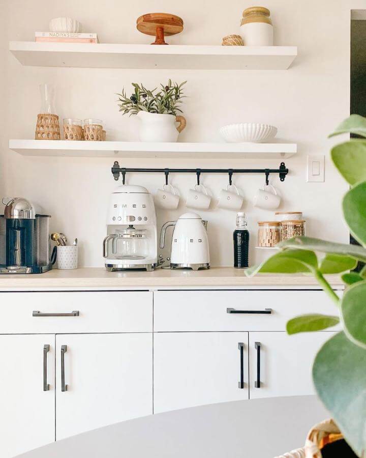 White minimalist coffee bar with floating shelves and hanging mugs from @honeynjoy. Clean and airy kitchen setup with SMEG appliances and plants.