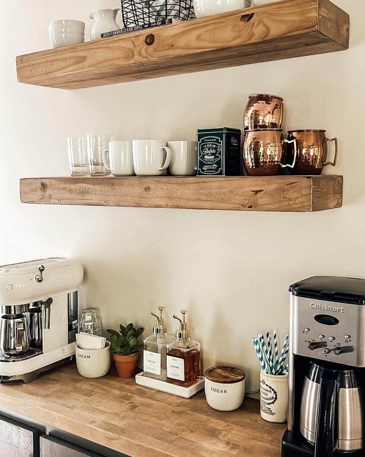 Warm wood floating shelves coffee bar setup with mugs, glassware, and copper cups by @everydaycottage. Inviting cozy kitchen corner idea.