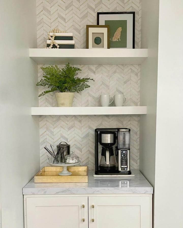 White marble countertop coffee nook with floating shelves and herringbone backsplash from @thissouthernhome. Cozy and stylish coffee corner with greenery and art.