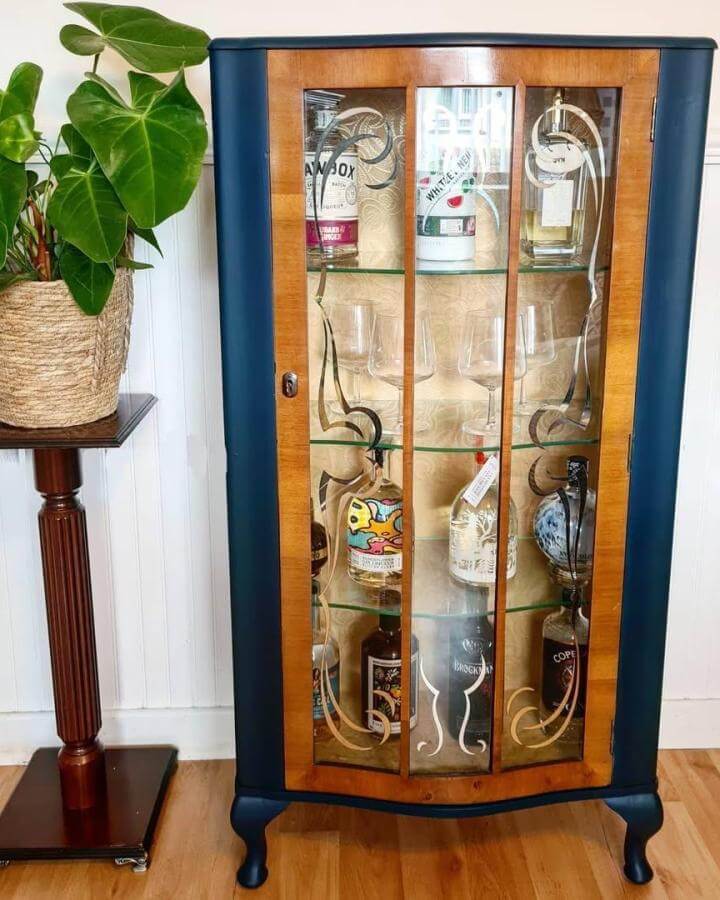 Vintage navy and wood diy drinks cabinet ideas by @glowups.furniture with etched glass and glass shelves in cozy room.