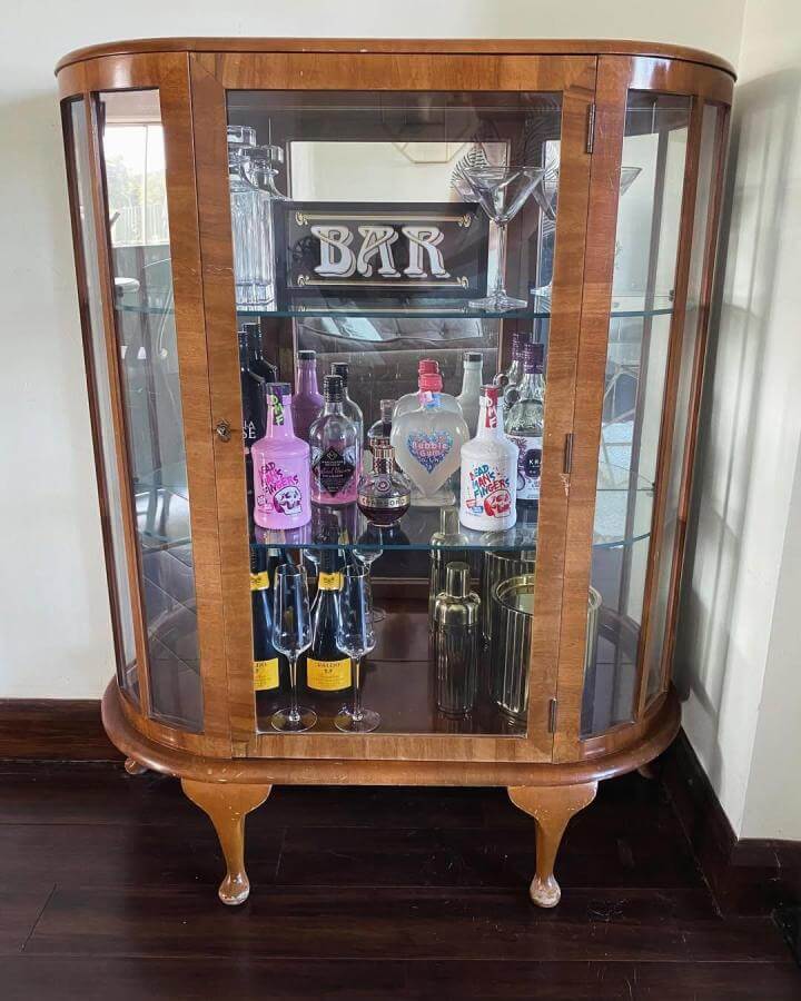 Curved glass vintage wooden drinks cabinet with mirrored back and warm tones from @house.number28 showcasing diy drinks cabinet ideas with bottles and glasses.