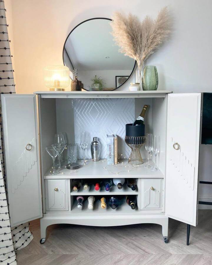 White painted Stag Minstrel diy drinks cabinet ideas with glassware, wine storage, pampas grass, and round mirror by @reloved_bybeverly. Elegant and cozy setup.