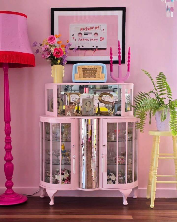 Pink vintage-style drinks cabinet with mirrored center and glass paneled doors surrounded by soft pink décor from @el_loves_colour.