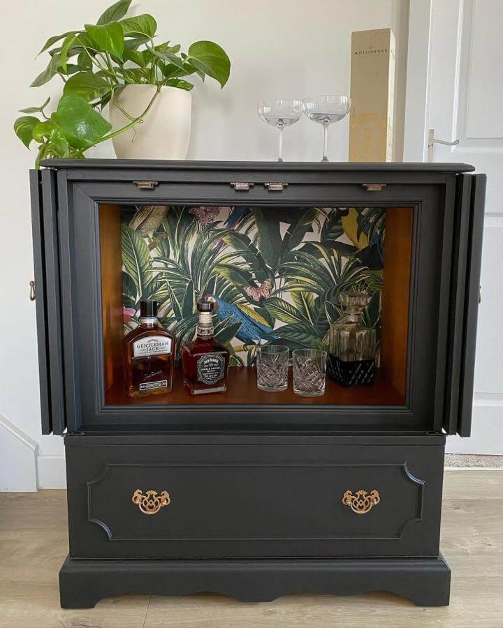 Black upcycled TV cabinet converted into diy drinks cabinet ideas with tropical wallpaper and gold handles. Elegant and stylish bar display.