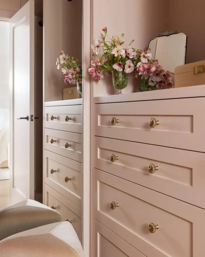 Blush pink built-in cabinetry from @arrowbuildersinc. Brass hardware and fresh flowers accent the storage system.