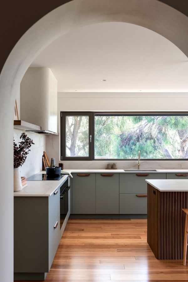 Sunlit kitchen, arched entryway, white cabinets, wooden floor, cozy ambiance.