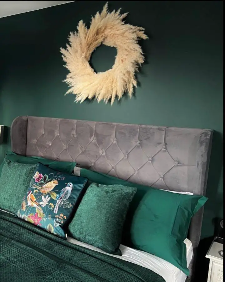 Moody emerald green bedroom ideas showcased with grey tufted headboard from @2_and_a_pug_at_no.2. Natural pampas wreath accent.