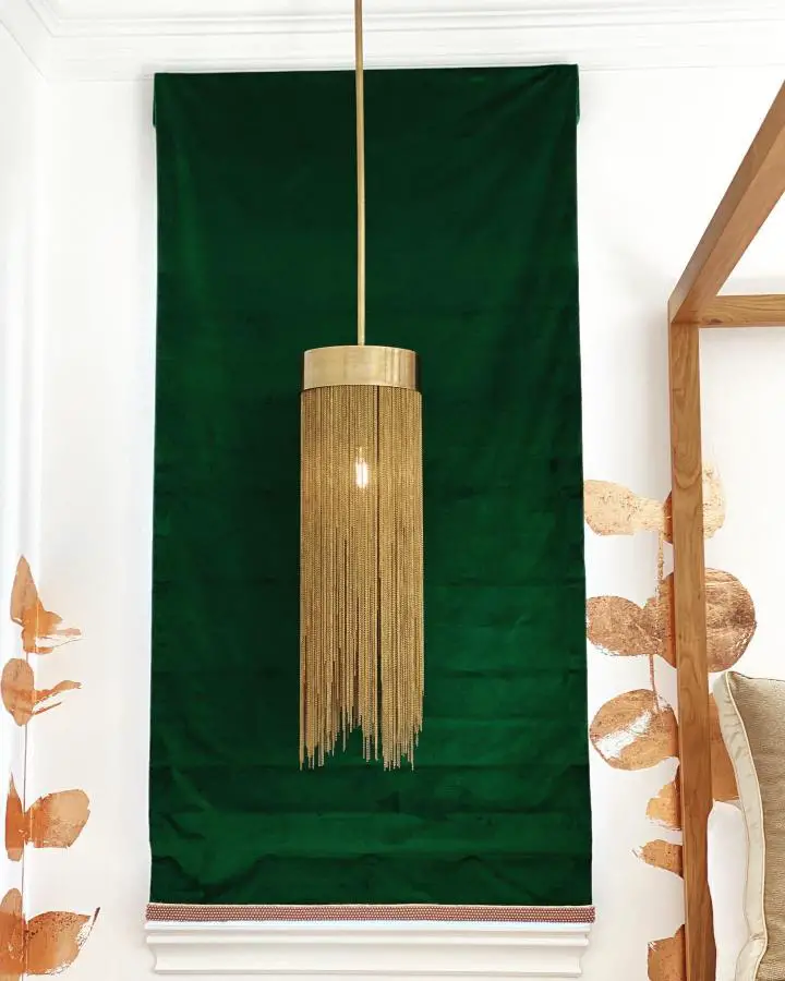Deep emerald fabric wall panel from @dianalombardinteriors. Golden fringe pendant light creates luxurious bedroom focal point.