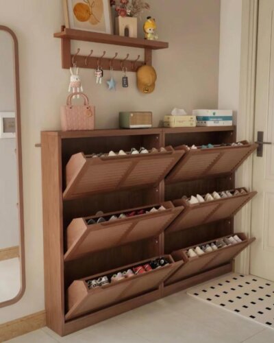 Warm wooden tilt-out shoe cabinet with hooks and shelf from @tiffany_design_studio in a cozy beige entryway space.