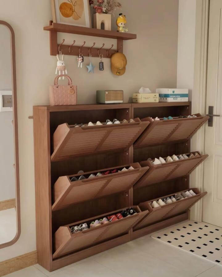 Warm wooden tilt-out shoe cabinet with hooks and shelf from @tiffany_design_studio in a cozy beige entryway space.