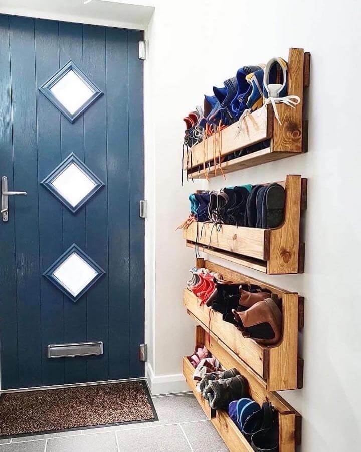 Wooden wall-mounted shoe rack in entryway with blue door and rustic style from @ourhometoyours storing various shoes neatly.