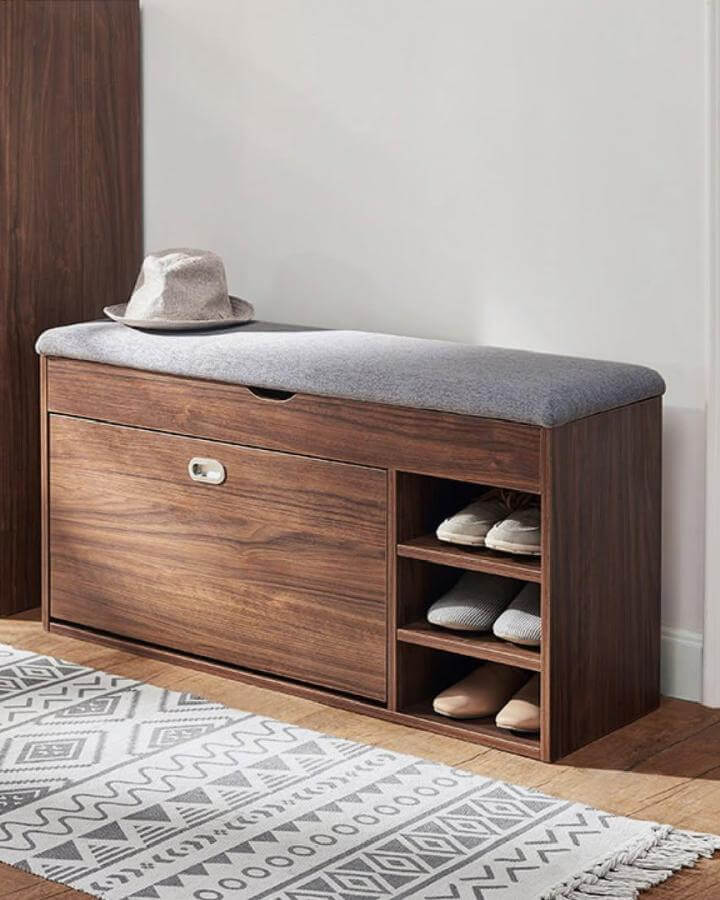 Warm walnut wood cushioned bench with built in shoe rack and open shelves for shoes from @mumuliving in a bright entryway space