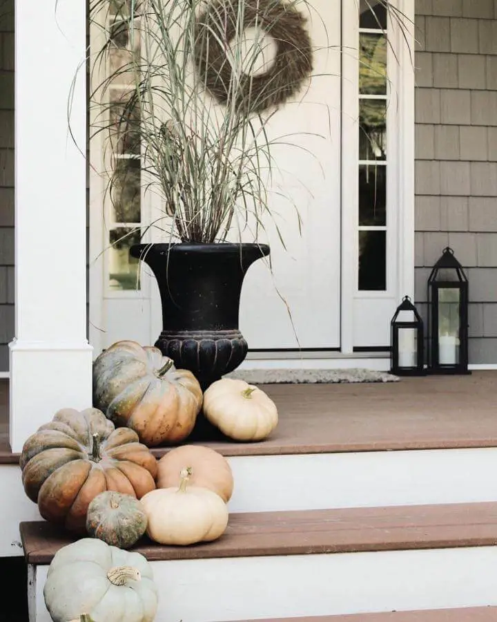 Black decorative urn with ornamental grasses showcasing fall front porch decor ideas from @sarah.g.johnson. Neutral pumpkins scattered on white porch steps.