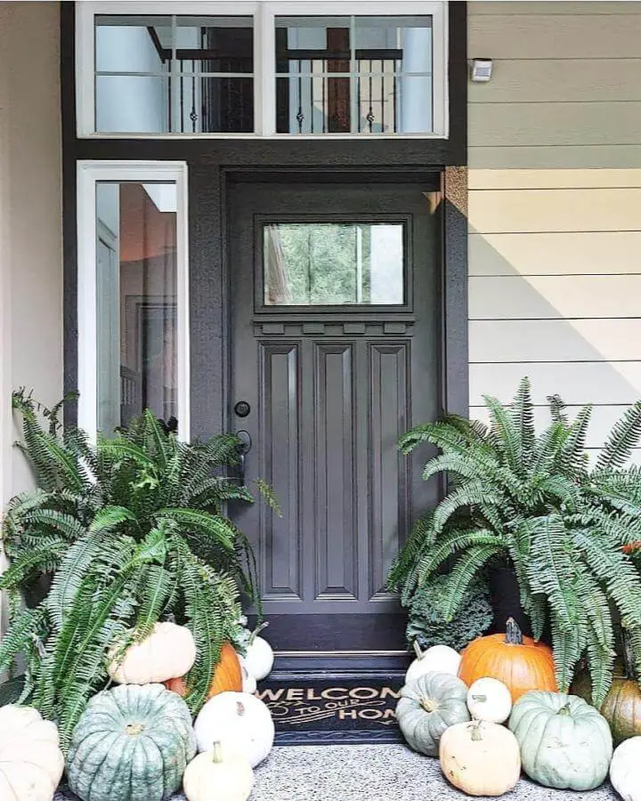 Neutral pumpkin display with ferns showcasing elegant fall front porch decor ideas from @houseofmargo. Cream and sage pumpkins arranged by dark door.