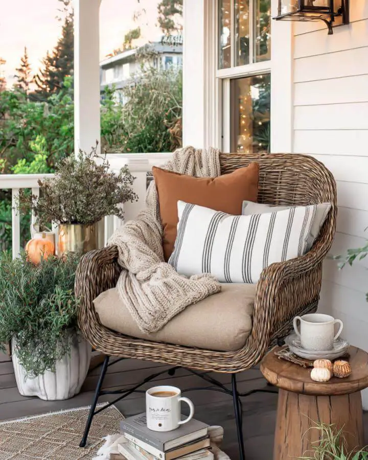 Wicker porch chair with autumn pillows and cozy throws creating inviting seating area.