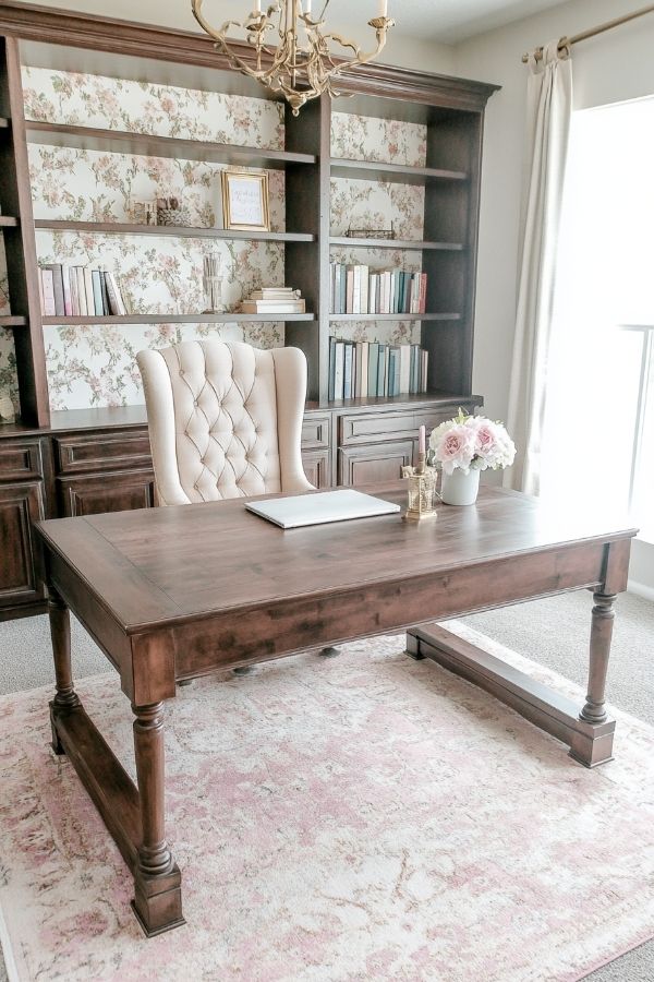 Feminine home office with pink decor, cozy chair, floral accents, soft lighting.