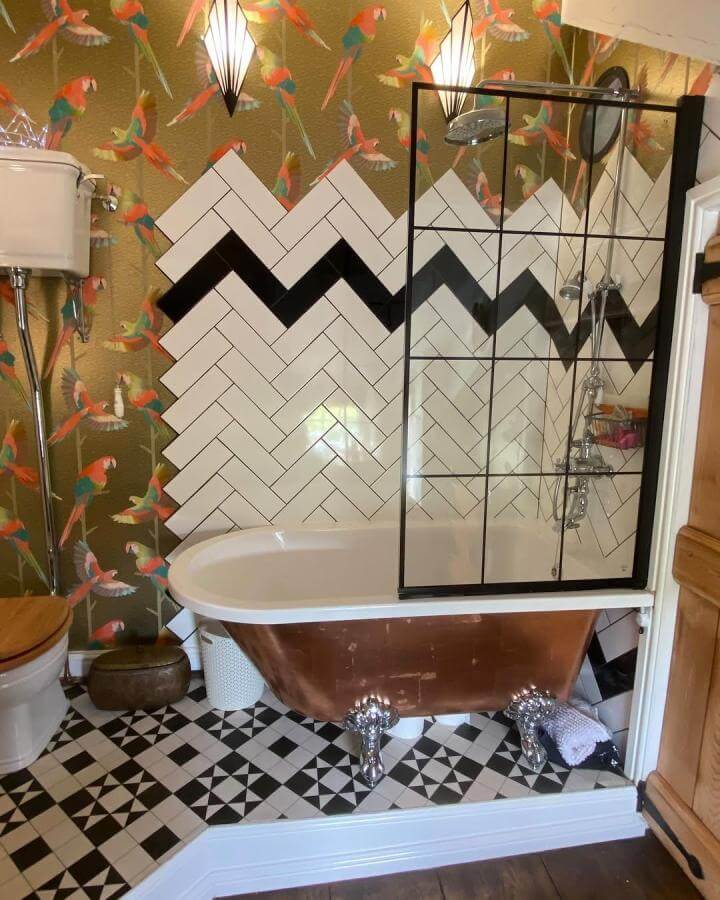 Copper clawfoot tub with black and white geometric tiles and vibrant parrot wallpaper in funky bathroom ideas by @escapingtohappiness. Creative pattern mix and tropical flair.