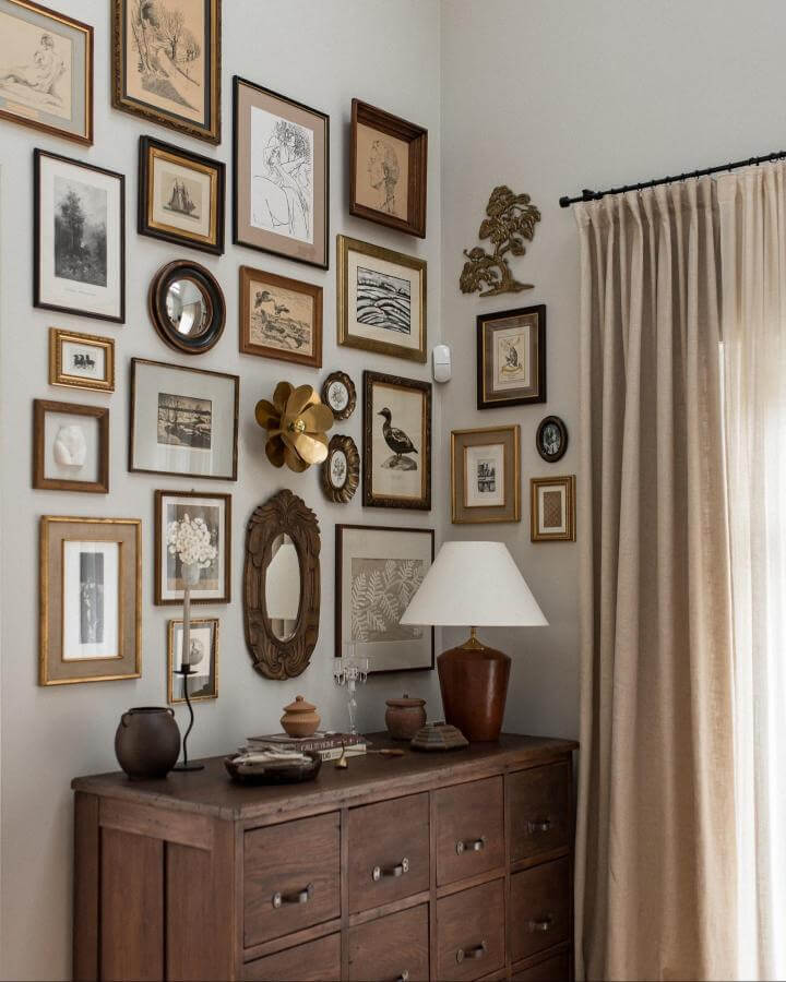 Warm eclectic vintage frames and brass accents above wooden chest from @annalovesneutrals create a cozy and inviting curated wall display.