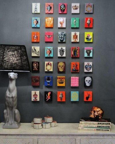 Colorful small art tiles arranged in a grid pattern on a dark grey wall with eclectic designs and bold pops of color.