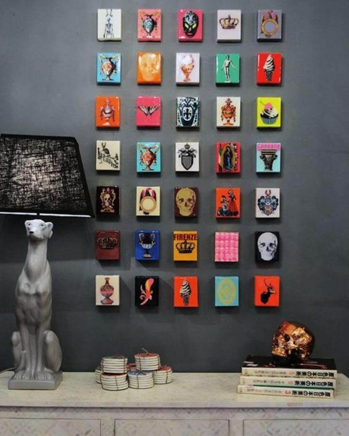 Colorful small art tiles arranged in a grid pattern on a dark grey wall with eclectic designs and bold pops of color.