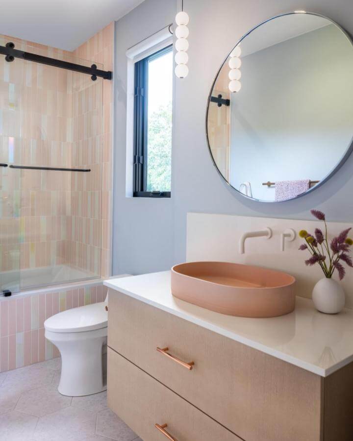 Soft pink tile bathroom with peach vessel sink and round mirror from @kuchar_studio showcasing girly bathroom ideas in a modern style