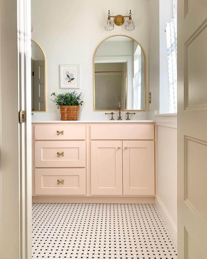 Soft pink cabinetry with gold bow knobs and brass mirrors in a girly bathroom ideas setting by @coppercolonial. Light, elegant, and charming design.