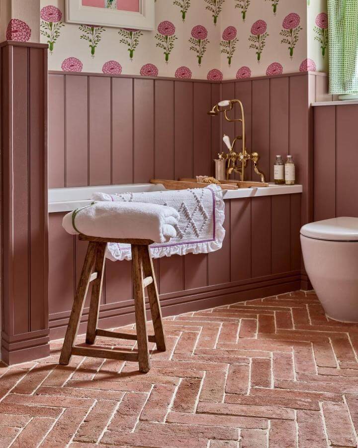 Muted rosewood paneling and floral wallpaper in a girly bathroom ideas space by @capietra with rustic wooden stool and brass fixtures
