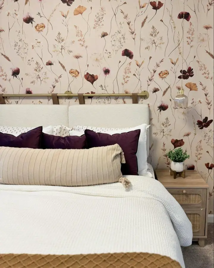 Botanical floral wallpaper bedroom from @_deeinteriors. Cream background with burgundy flowers, plum pillows, neutral bedding.