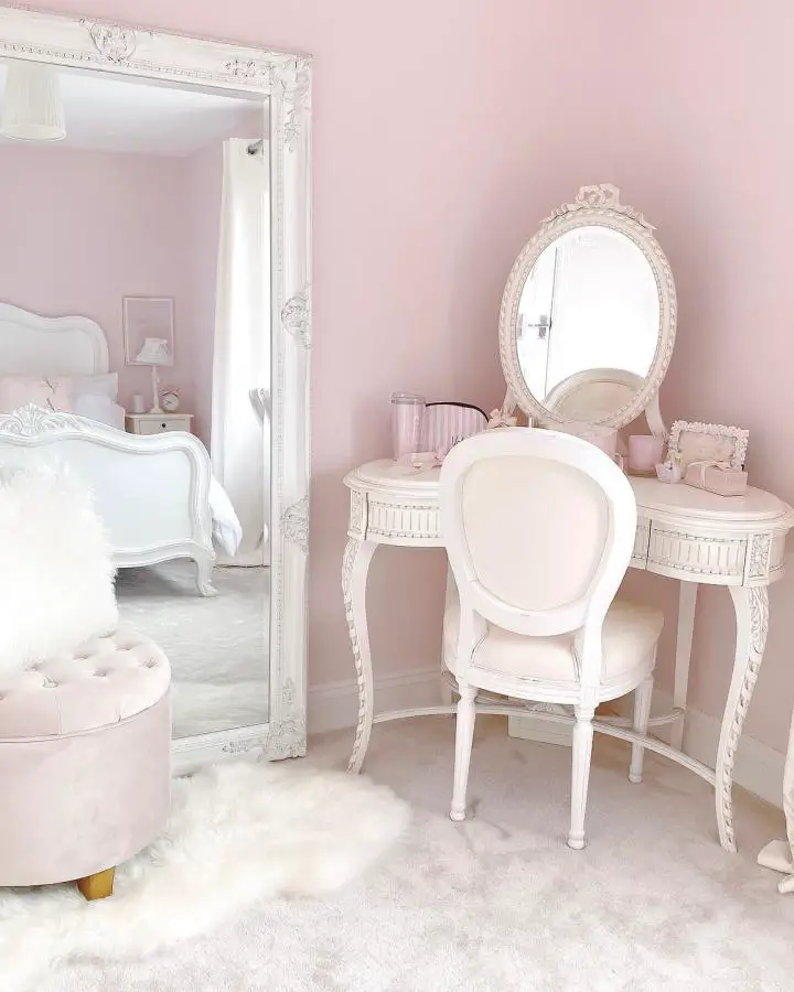 Ornate white vanity table from @catherine.mw. Vintage-style furniture against blush pink walls with plush white rug.