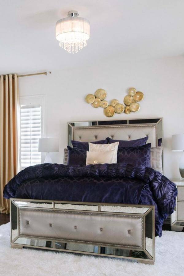 Mirrored tufted bed frame from @nikkiklughdesign. Navy velvet bedding with crystal chandelier above.
